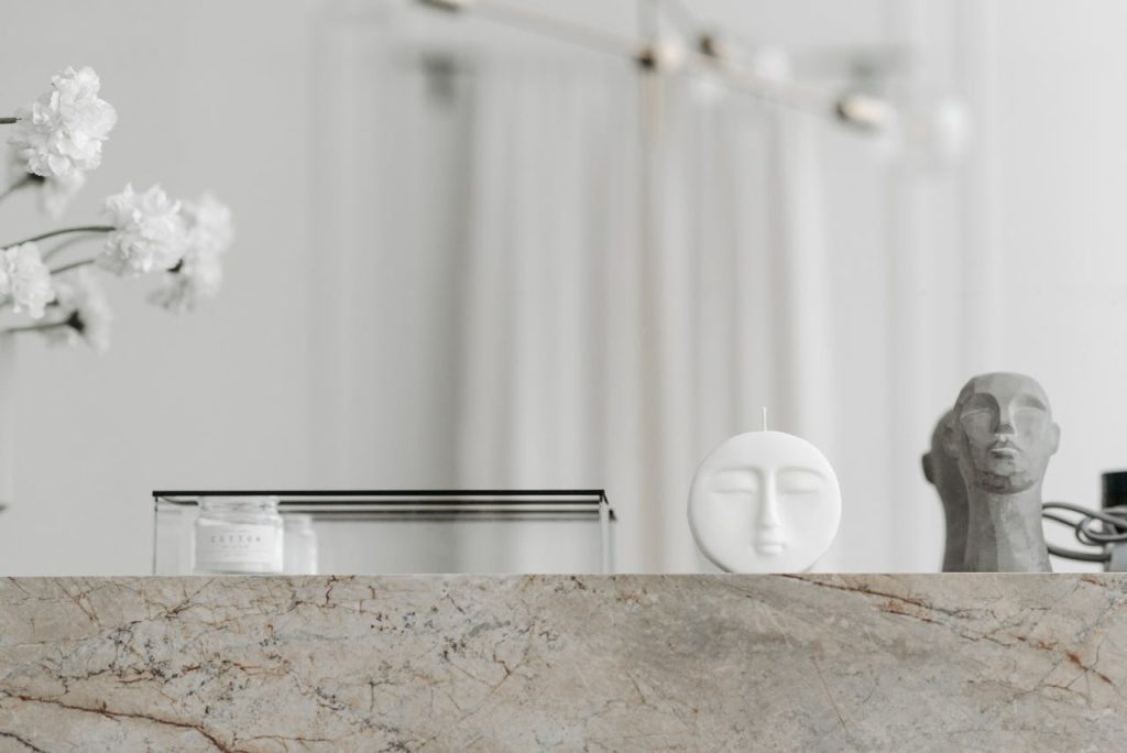 Modern minimalist arrangement with sculptures and a candle on a marble surface, exuding elegance.