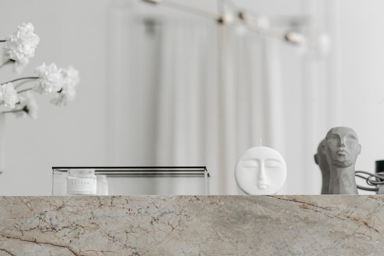 Modern minimalist arrangement with sculptures and a candle on a marble surface, exuding elegance.